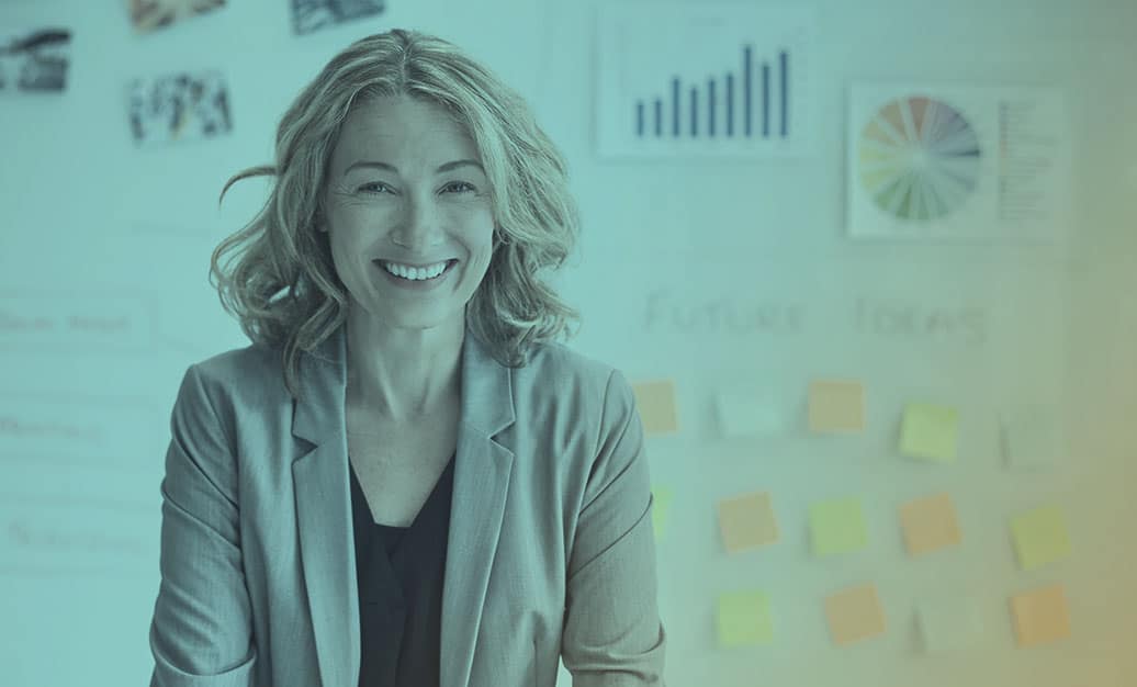 Business executive smiling in front of a white board with data graphs and post-its stuck to it