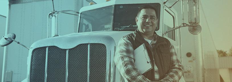 A man in checkered shirt and vest in front of a his transport truck