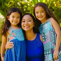 A woman and her two young daughters smiling at camera