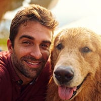 Thumbnail of a man crouched beside his golden retriever looking at the camera