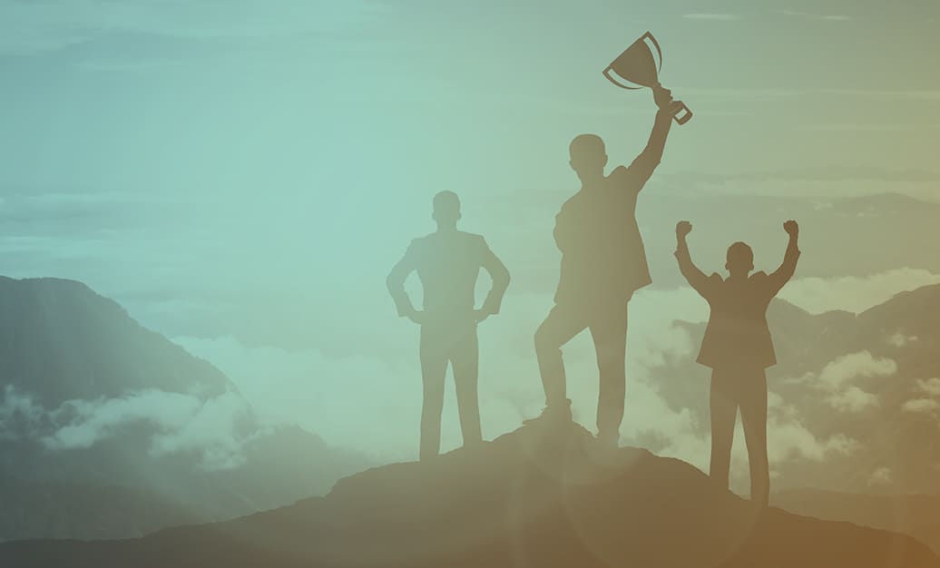 Three silhouettes standing on a mountain peak with the middle silhouette holding up a trophy