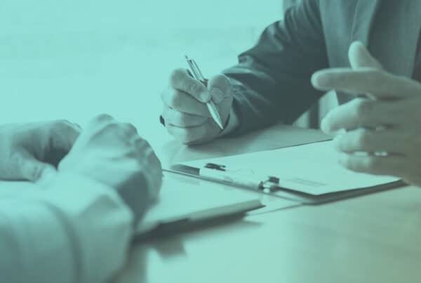 2 business men at a desk reviewing numbers on a clipboard
