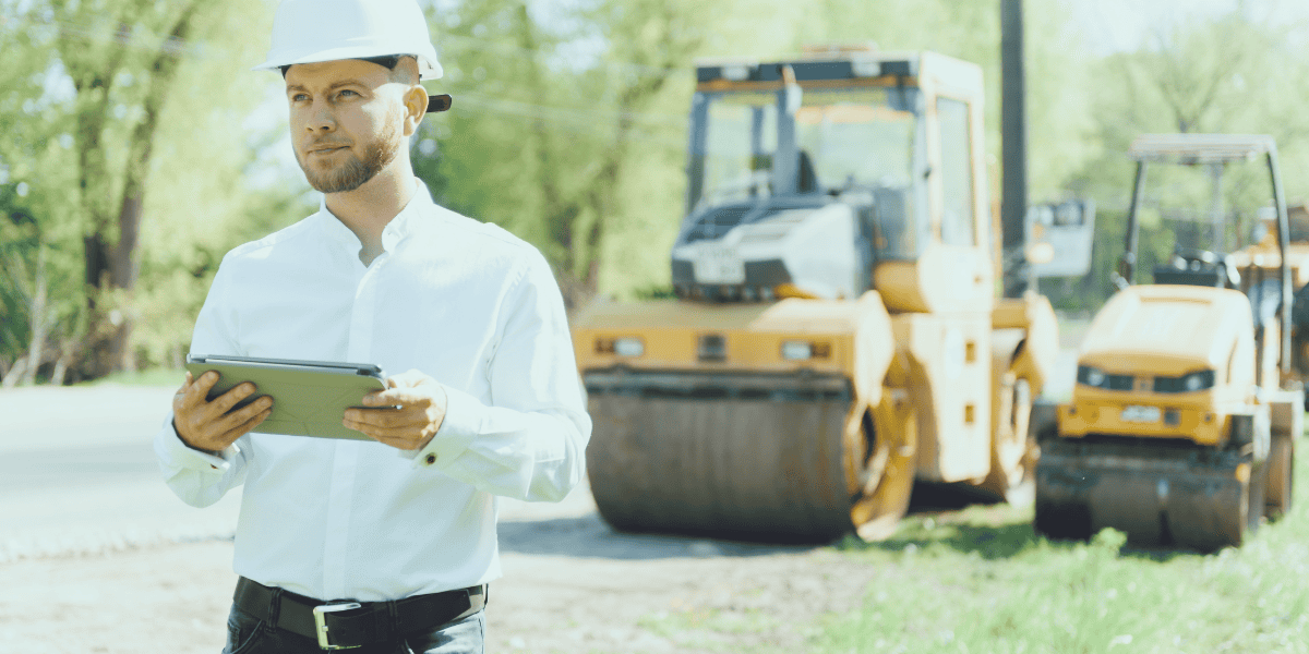 A construction worker reviewing his clipboard with his assets in the background