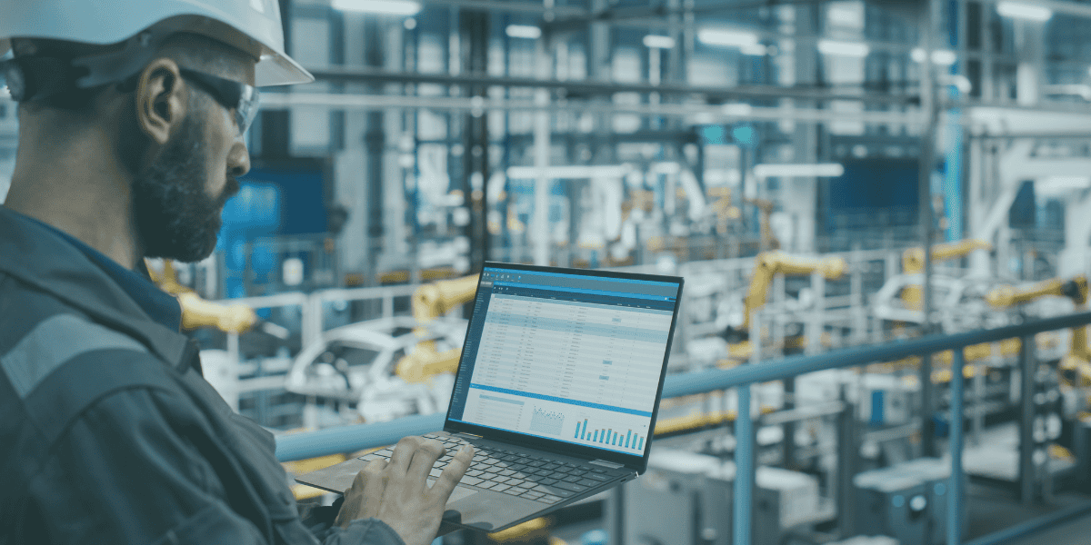 A man looking at his laptop in a manufacturing plant\