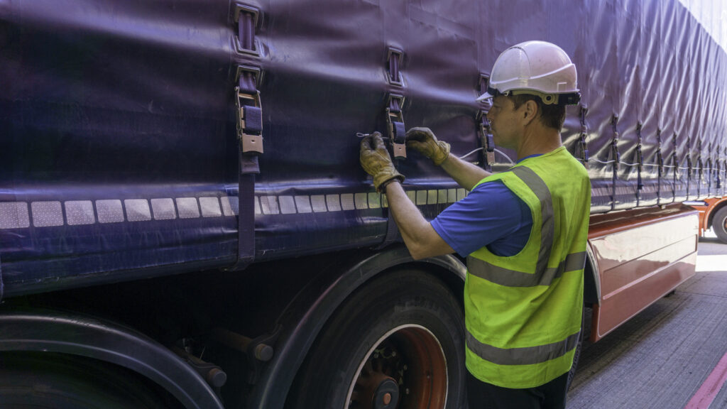 Man strapping down a tarp on a transportation vehicle.