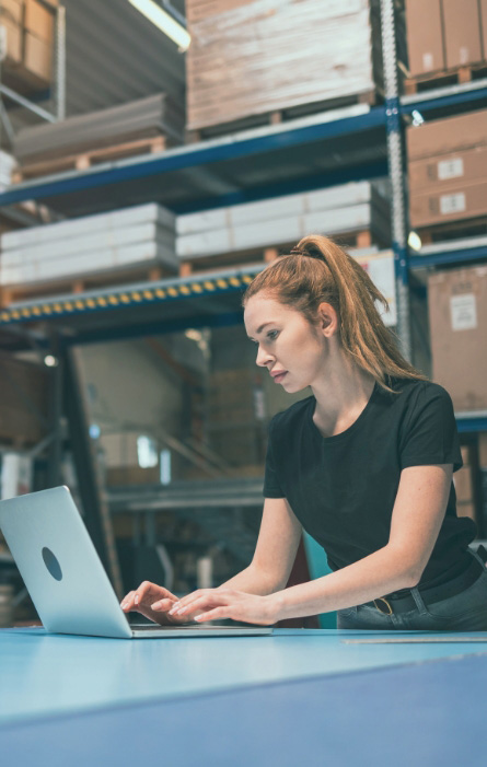 Consumer goods business owner in a warehouse reviewing financing on her laptop