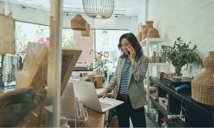 Business woman on the phone and looking at her laptop in her shop.